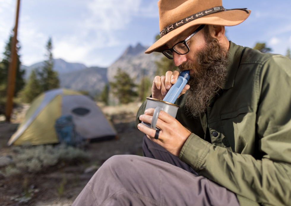 Mężczyzna filtruje wodę filtrem słomkowym LifeStraw Peak Personal podczas campingu