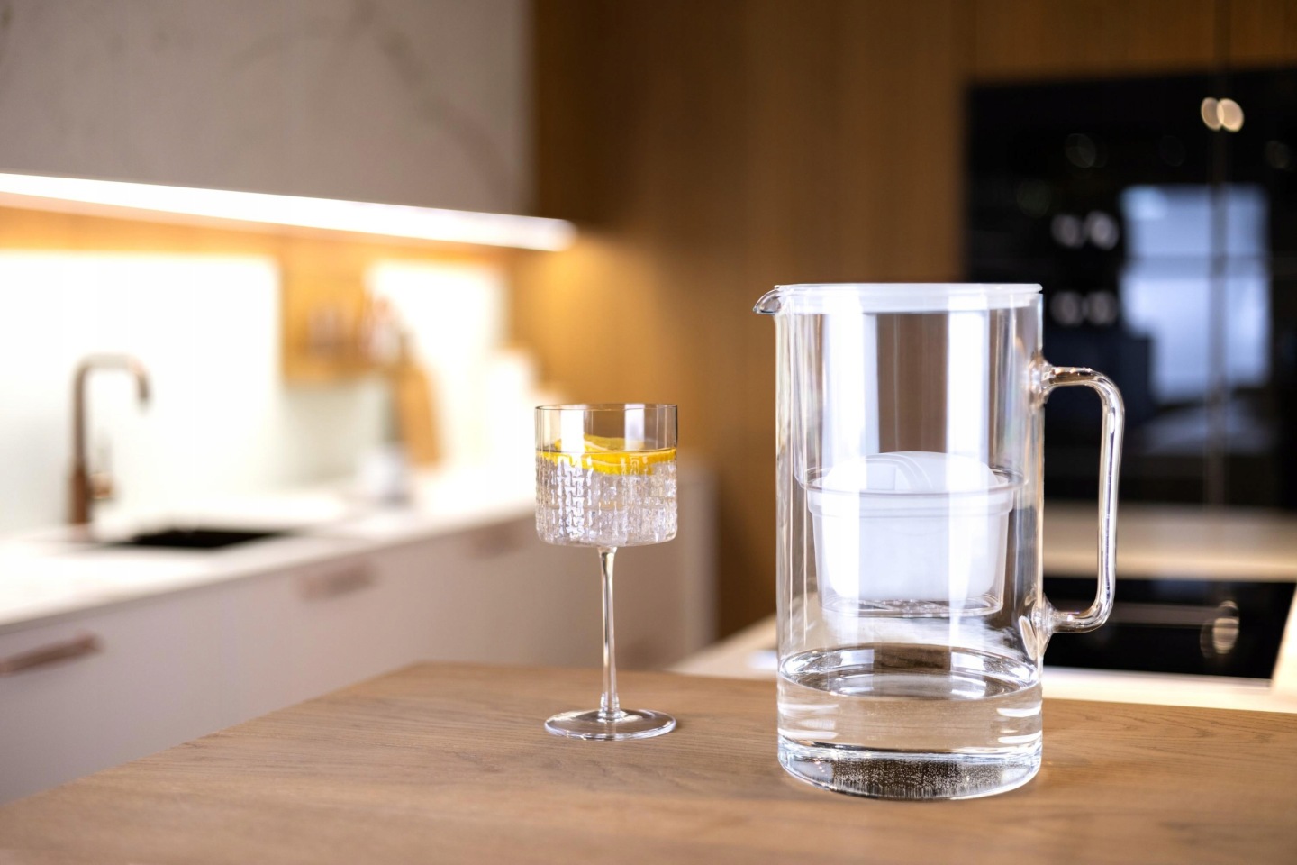 Szklany dzbanek z&nbsp;białą pokrywką Wessper D2 na blacie kuchennym obok kieliszka oczyszczonej wody