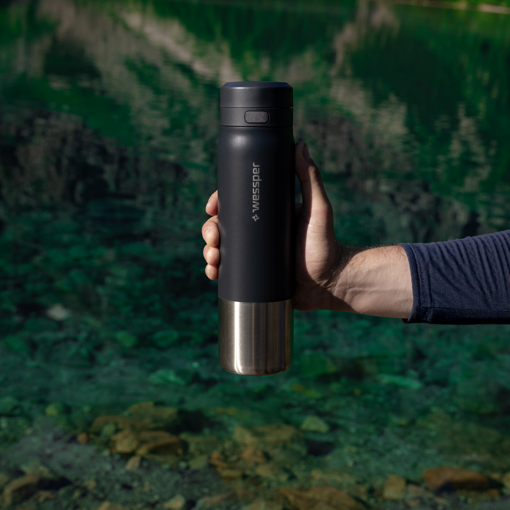 Prezentacja stalowego bidonu na wodę z filtrem - mężczyzna trzyma butelkę nad czystą górską wodą