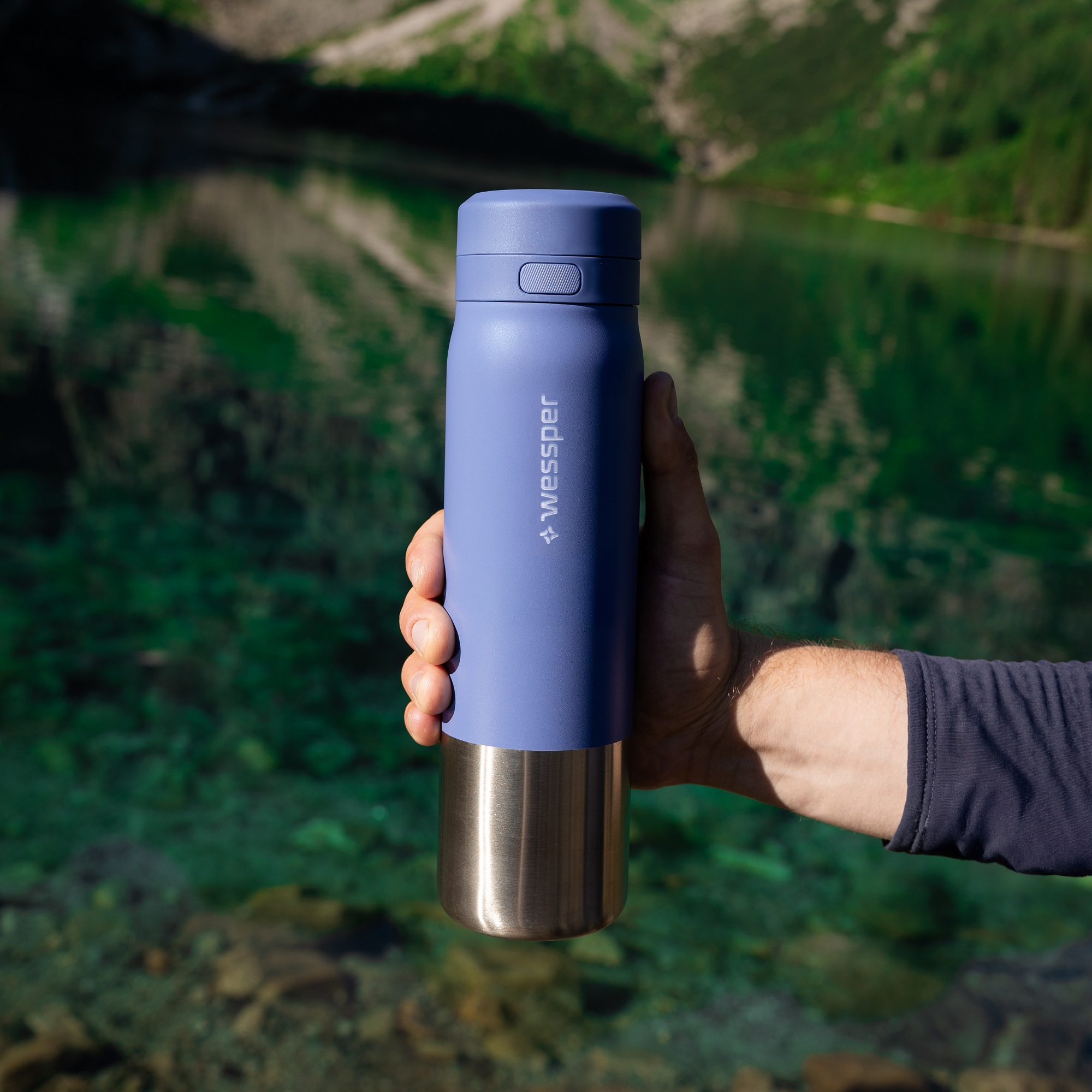 Mężczyzna prezentuje niebieską stalowa butelkę WESSPER B2 w&nbsp;terenie