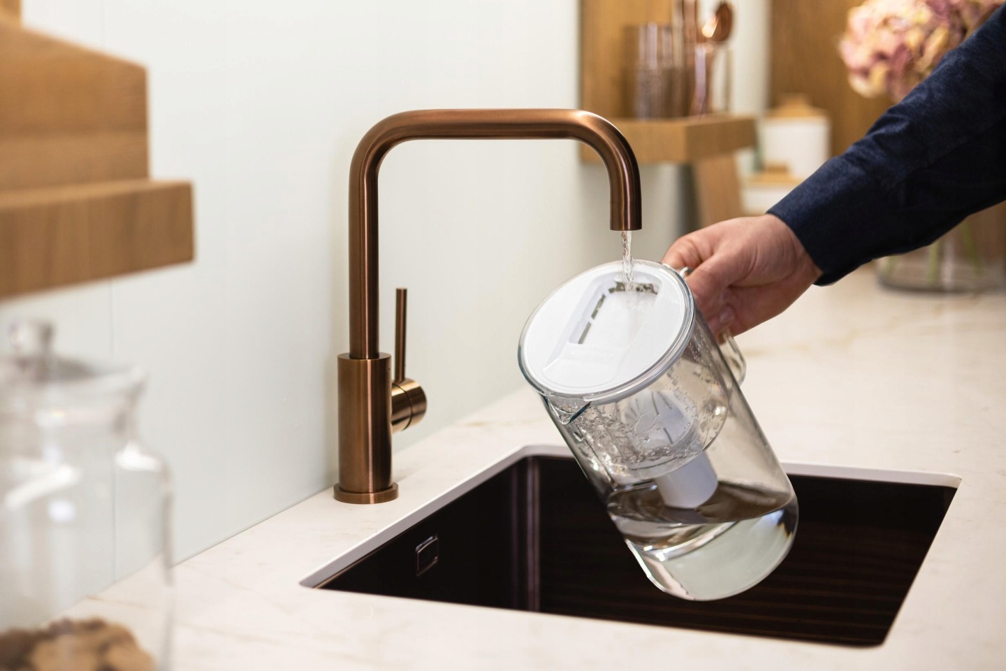 Mężczyzna napełnia dzbanek filtrujący Wessper D2 BOROSILICATE wodą z&nbsp;eleganckiej kuchennej wylewki