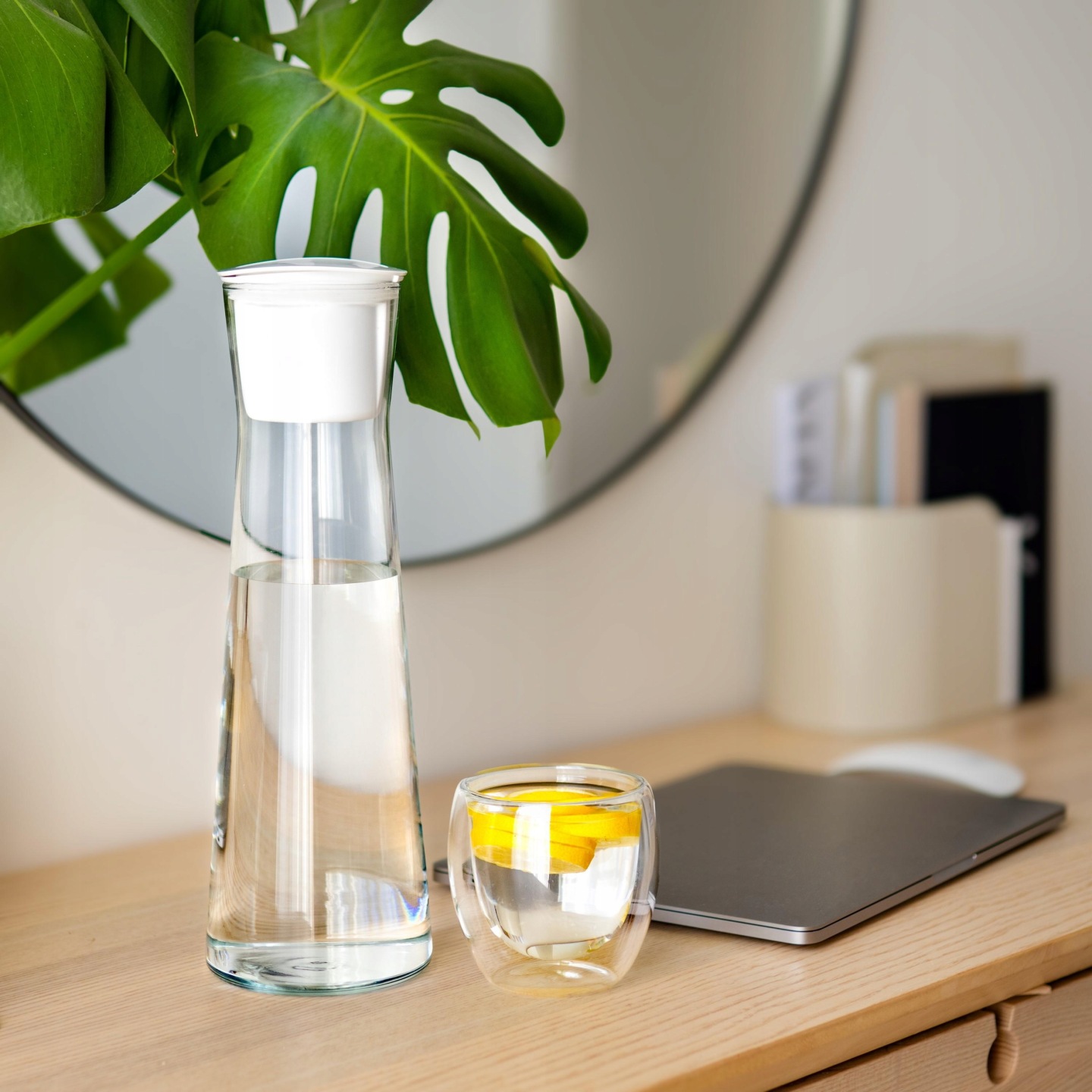 Karafka na biurku w biurze - na blacie obok czysta przefiltrowana woda z cytryną i złożony laptop