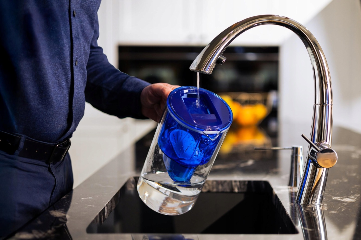 Mężczyzna uzupełnia dzbanek Wessper w granatowym kolorze wodą z baterii kuchennej
