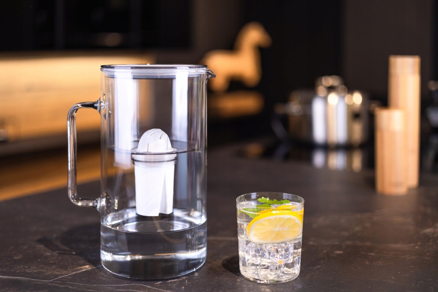 Szary dzbanek Wessper ze szkła borokrzemowego na blacie kuchennym obok szklanki z&nbsp;przefiltrowaną wodą