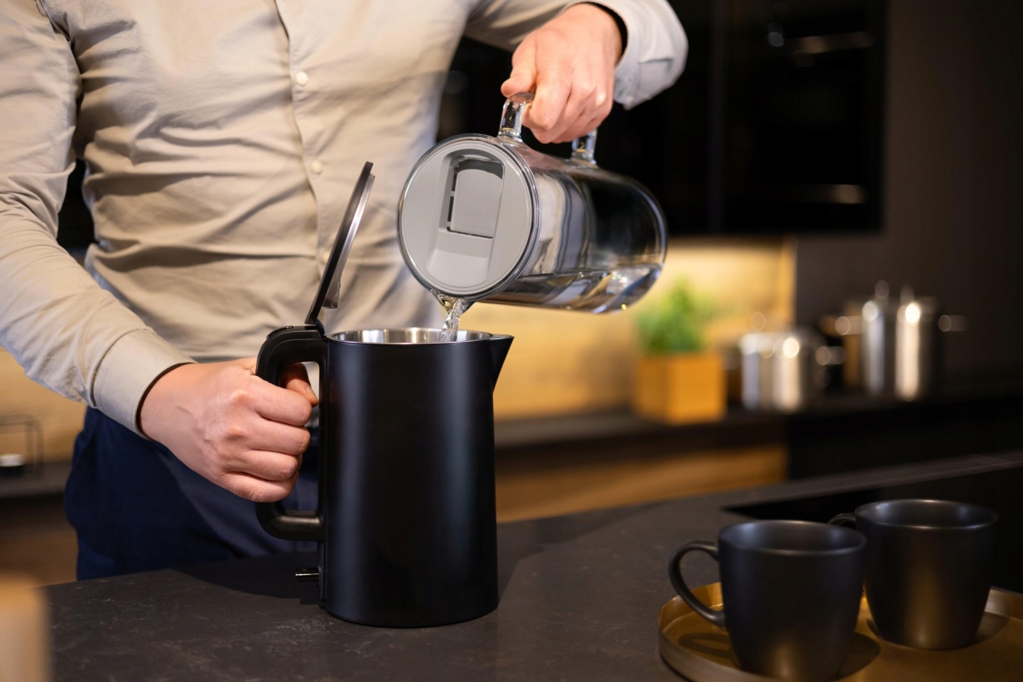 Mężczyzna napełnia czajnik wodą z&nbsp;dzbanka szklanego Wessper