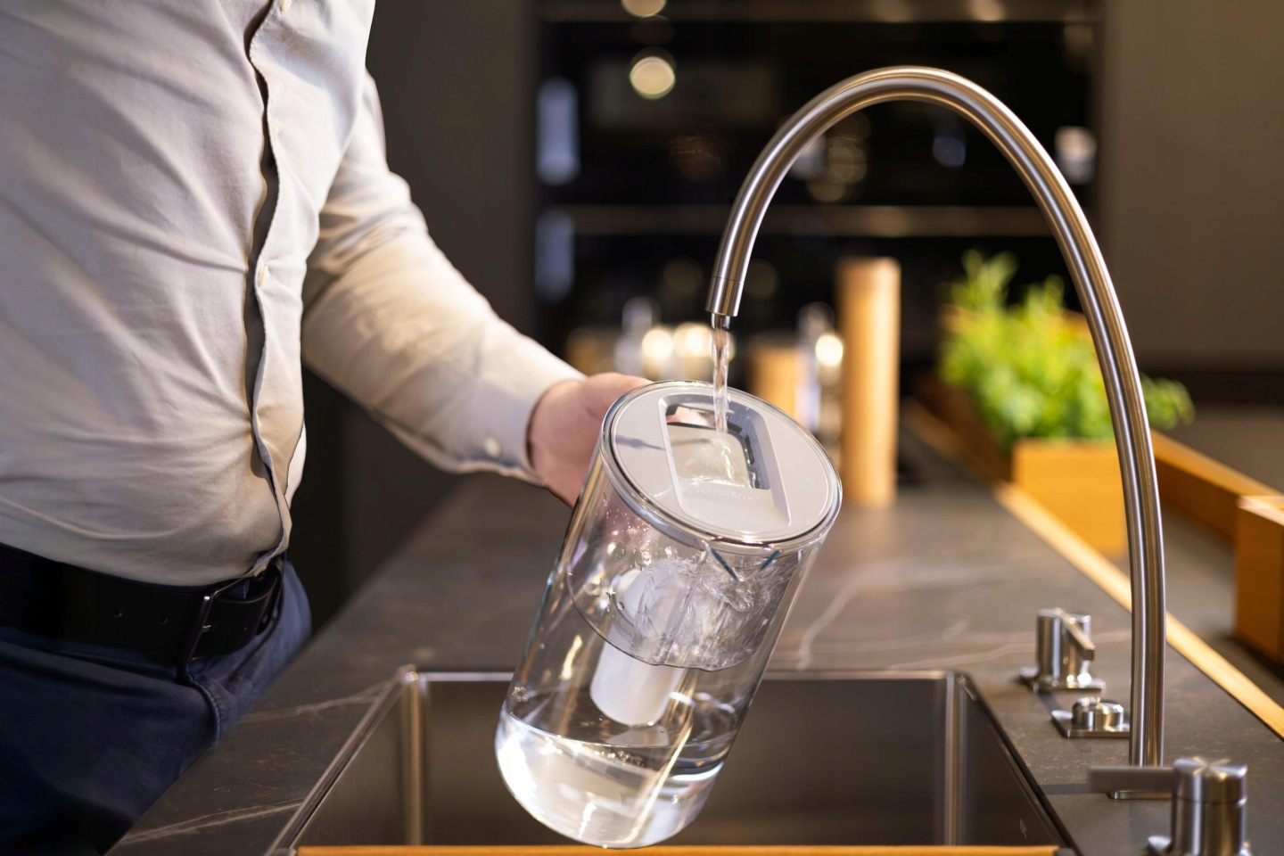 Mężczyzna napełnia szklany dzbanek Wessper wodą z&nbsp;baterii kuchennej